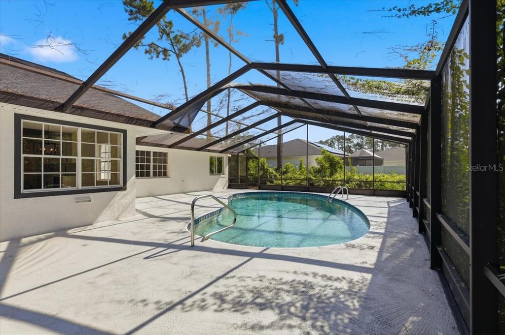 A swimming pool sits on a concrete patio enclosed by a screened-in lanai structure — 2 ELDER PLACE, PALM COAST, FL