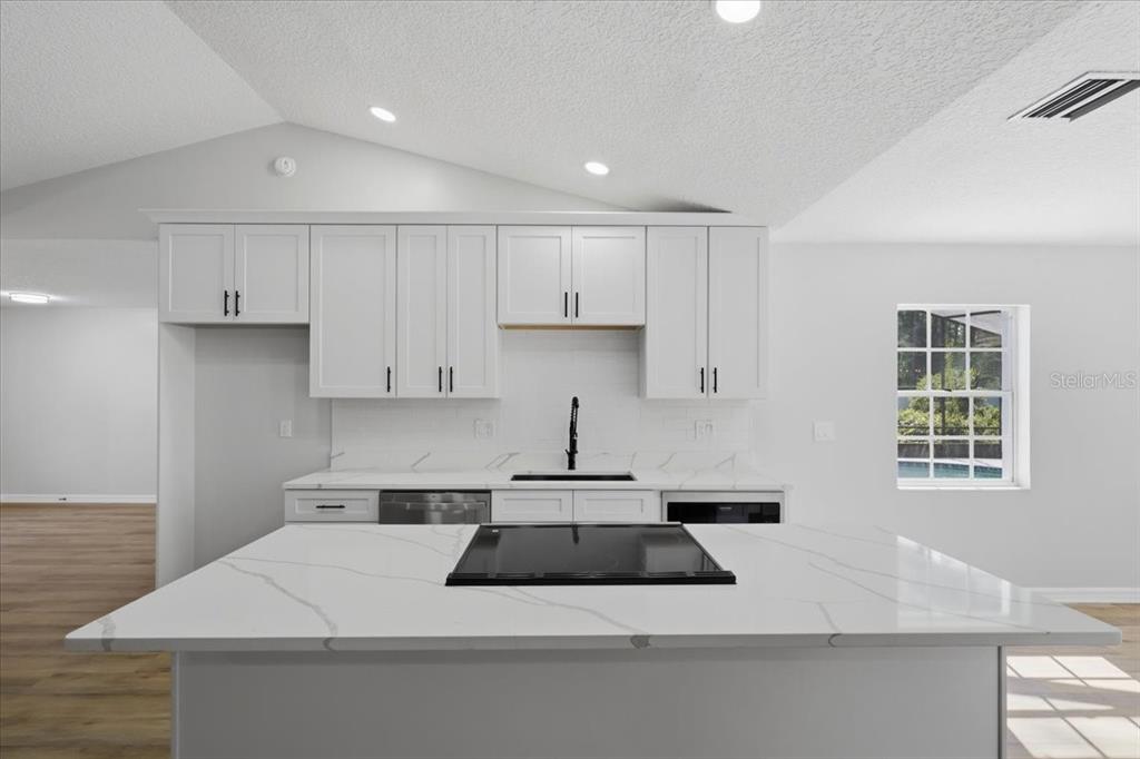 A modern kitchen features white cabinetry, a marble-patterned island with a cooktop, and white walls — 2 ELDER PLACE, PALM COAST, FL