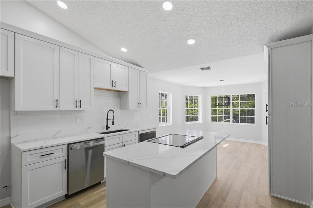 A modern kitchen features white cabinets, a marble-topped island with a cooktop, and stainless appliances — 2 ELDER PLACE, PALM COAST, FL