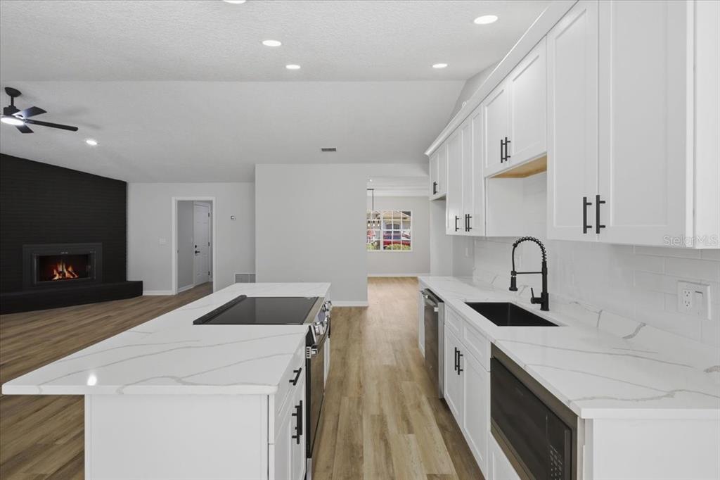A modern kitchen features white cabinets, quartz countertops, a center island, and a black fireplace — 2 ELDER PLACE, PALM COAST, FL