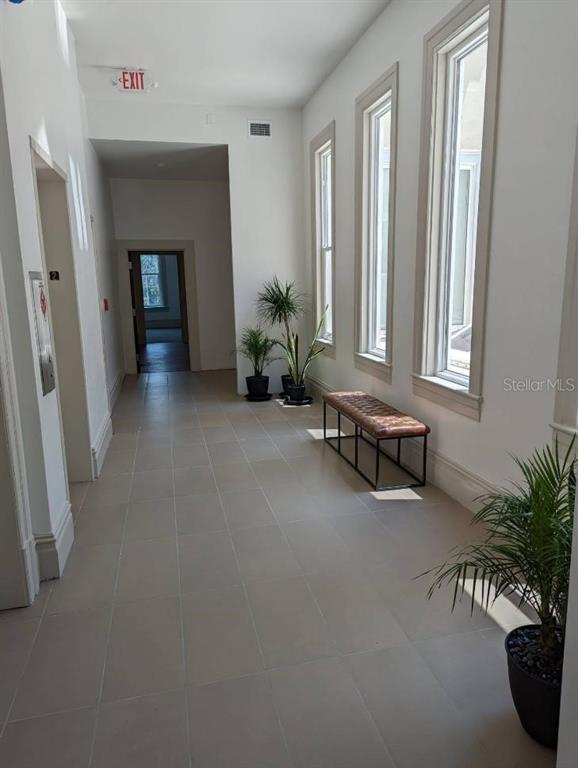 A bright hallway features light tile flooring, tall windows, a leather bench, and potted plants — 1718 E 7TH AVENUE UNIT 201-C & E, TAMPA, FL
