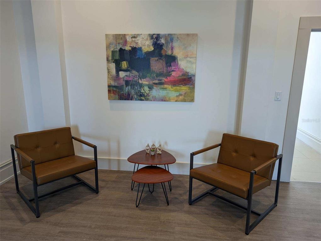 Two brown leather armchairs flank a small tiered wooden table beneath an abstract painting — 1718 E 7TH AVENUE UNIT 201-C & E, TAMPA, FL