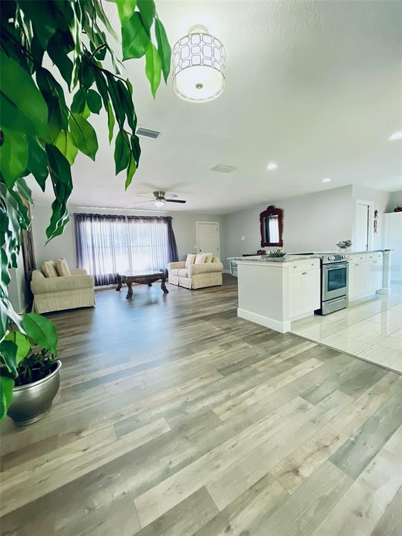 This open-concept living area features wood-look flooring, a kitchen island, and a seating area — 1643 SAXON BOULEVARD, DELTONA, FL