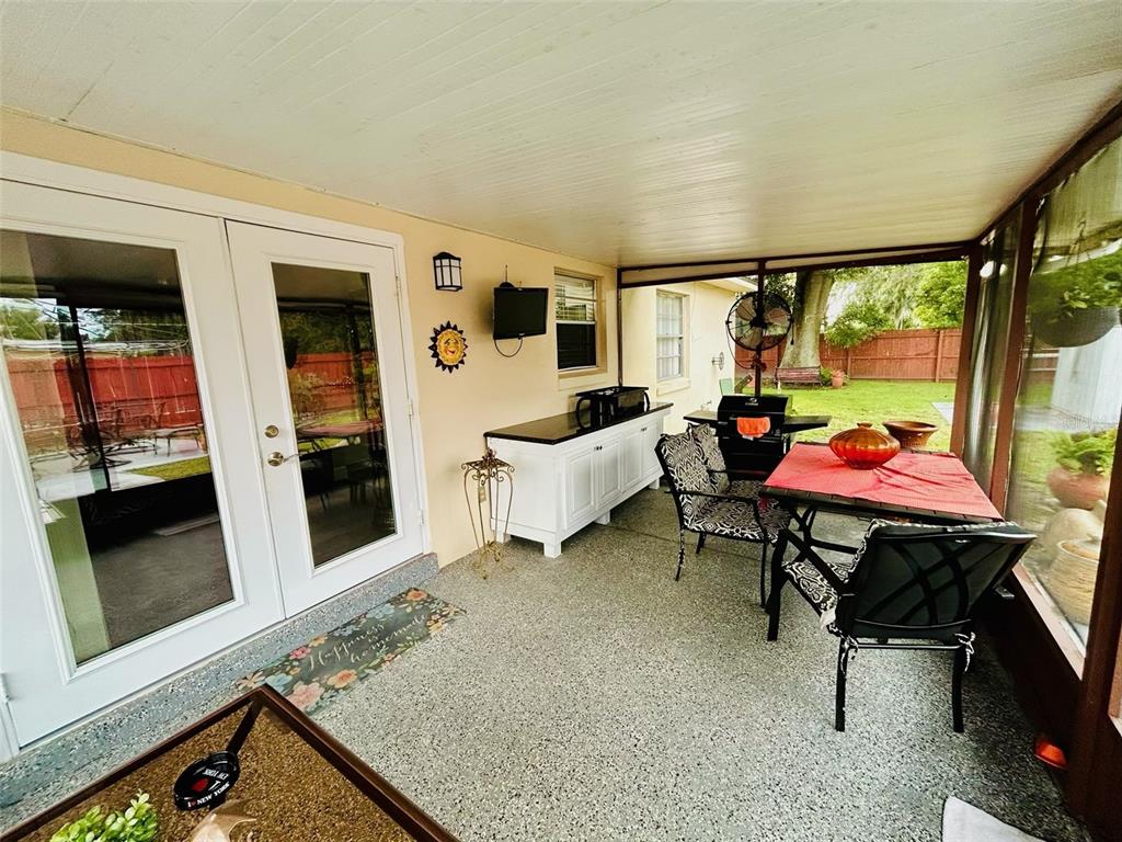 A covered patio features a dining set, a grill, a white cabinet, and glass doors — 1643 SAXON BOULEVARD, DELTONA, FL