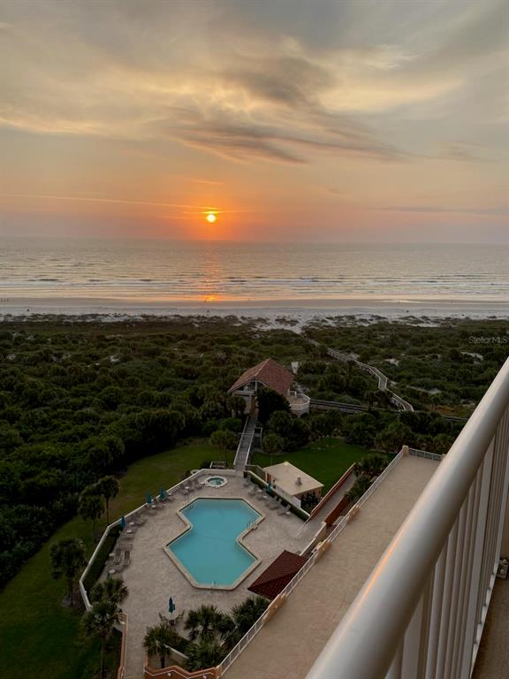 An elevated view of a swimming pool, coastal vegetation, and a beach at sunset — 257 MINORCA BEACH WAY UNIT 1202, NEW SMYRNA BEACH, FL
