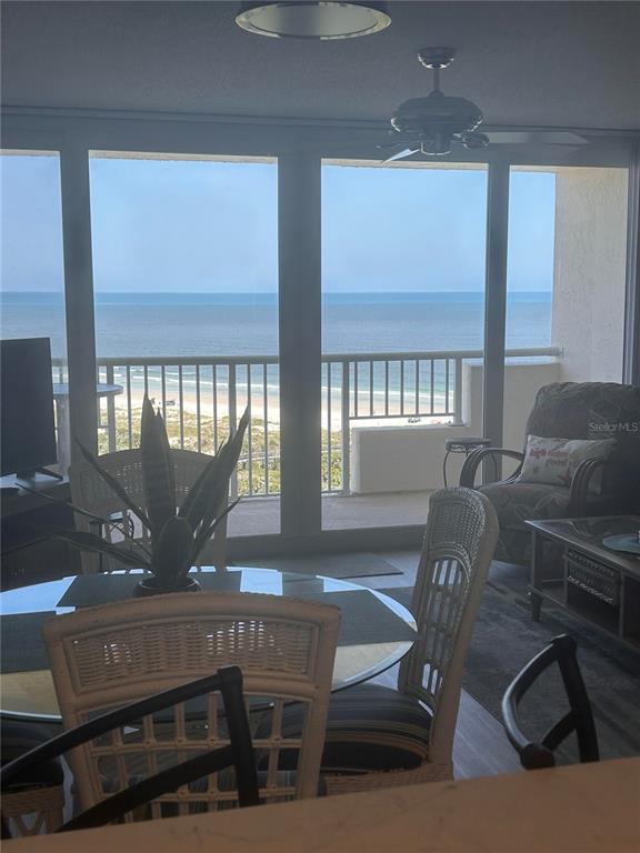 A dining area with a glass table and wicker chairs overlooks the ocean from a balcony — 257 MINORCA BEACH WAY UNIT 1202, NEW SMYRNA BEACH, FL