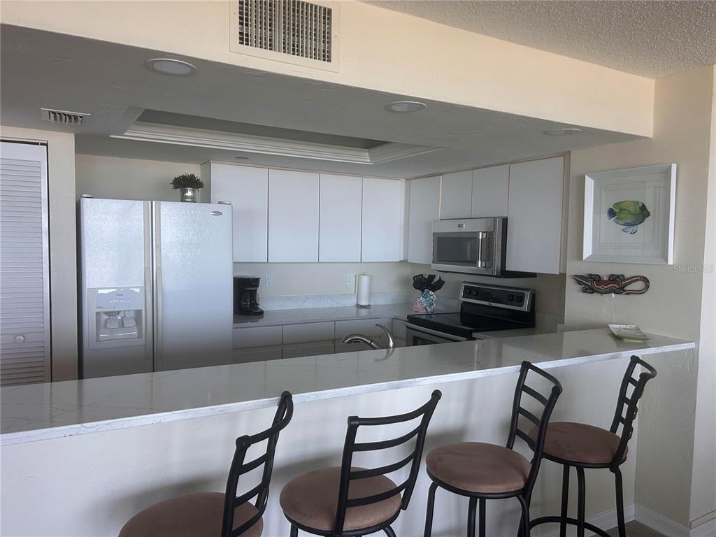 A kitchen with white cabinets, stainless steel appliances, and a breakfast bar with three stools — 257 MINORCA BEACH WAY UNIT 1202, NEW SMYRNA BEACH, FL