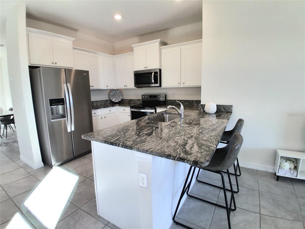 A kitchen features white cabinets, stainless steel appliances, and a dark granite-topped island — 8072 PENROSE PLACE, WILDWOOD, FL