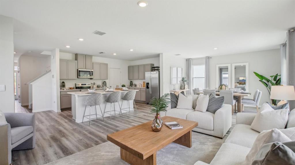 An open-concept living room and kitchen featuring light wood flooring, gray cabinetry, and neutral furniture — 35484 SUNFLOWER HILL DRIVE, ZEPHYRHILLS, FL