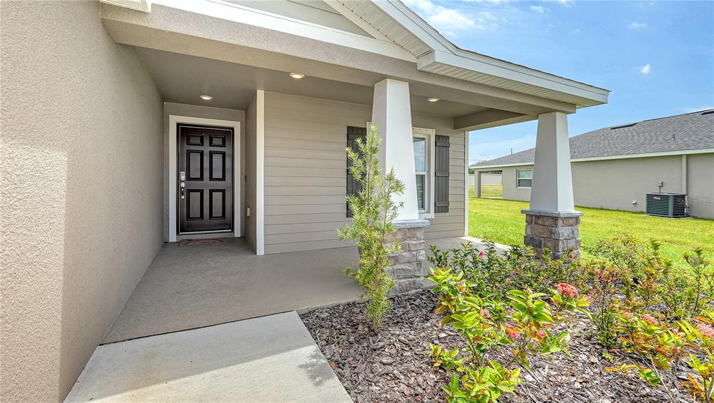 A covered front porch features a dark door, stone-based columns, and a small landscaped garden — 2512 58TH CIRCLE E, PALMETTO, FL