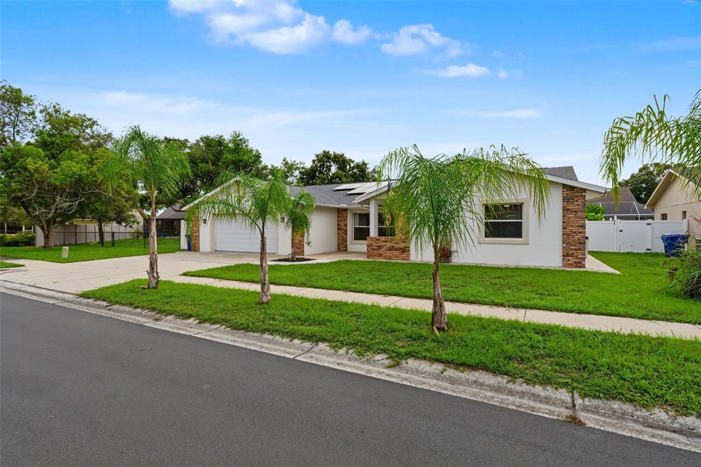 A single-story house with a white stucco facade, brick accents, a two-car garage, and palm trees — 4607 SAWGRASS BOULEVARD, NEW PORT RICHEY, FL