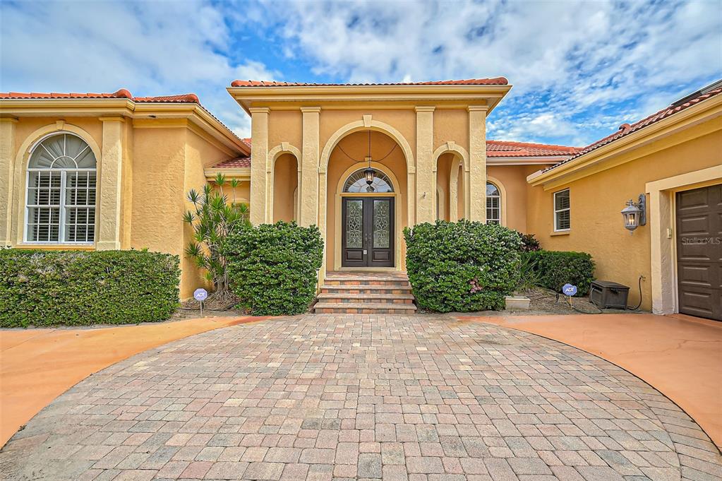 A yellow stucco house features a paved driveway, arched entryway, and a dark double door — 909 MACEWEN DRIVE, OSPREY, FL