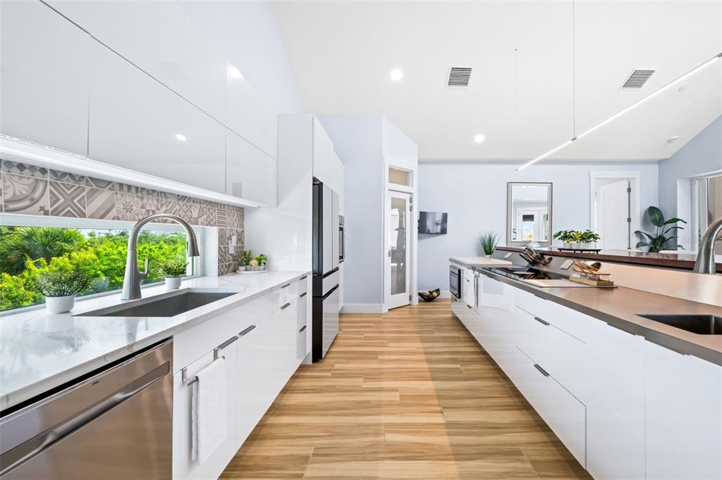 A modern kitchen features white cabinetry, a patterned backsplash, stainless steel appliances, and wood flooring — 10101 EAGLE PRESERVE DRIVE, ENGLEWOOD, FL