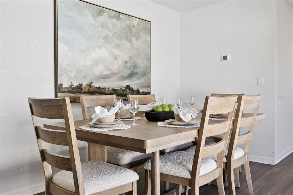A dining room features a wooden table with chairs, white shiplap walls, and landscape wall art — 1770 GRANDIOSE DRIVE, LAKE HAMILTON, FL