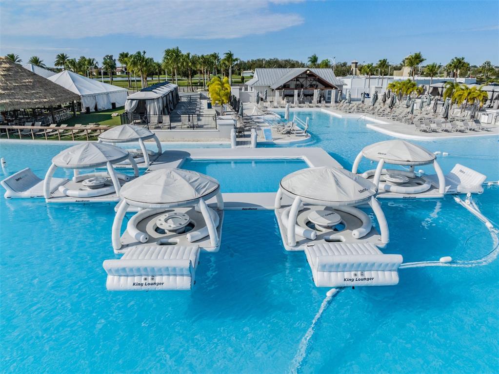 An aerial view of a resort-style swimming pool featuring several floating cabanas and lounge platforms — 7328 POOL COMPASS LOOP, WESLEY CHAPEL, FL