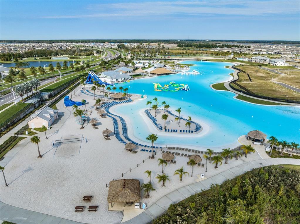 An aerial view shows a large turquoise swimming lagoon with sandy beaches and palm trees — 7328 POOL COMPASS LOOP, WESLEY CHAPEL, FL