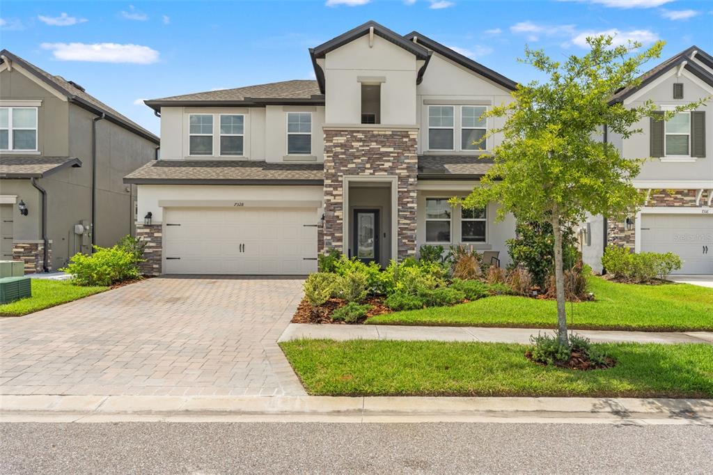 A two-story suburban house with a stone-accented facade, a paved driveway, and a front lawn — 7328 POOL COMPASS LOOP, WESLEY CHAPEL, FL