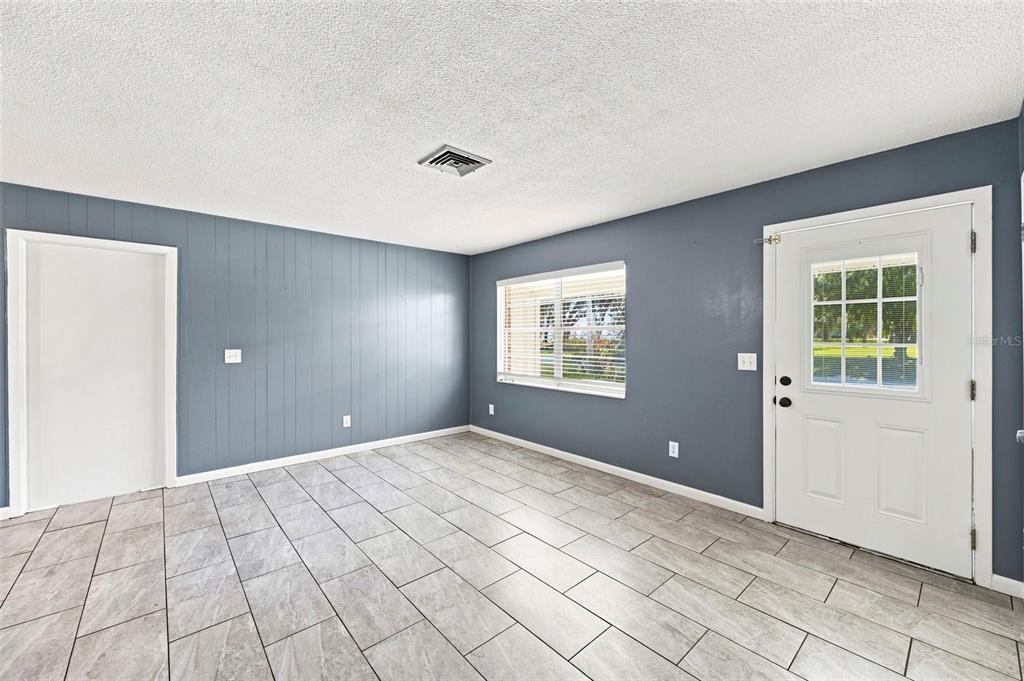 An empty room with gray paneled walls, tile flooring, a window, and a white door — 1655 N FLORAL AVENUE, BARTOW, FL