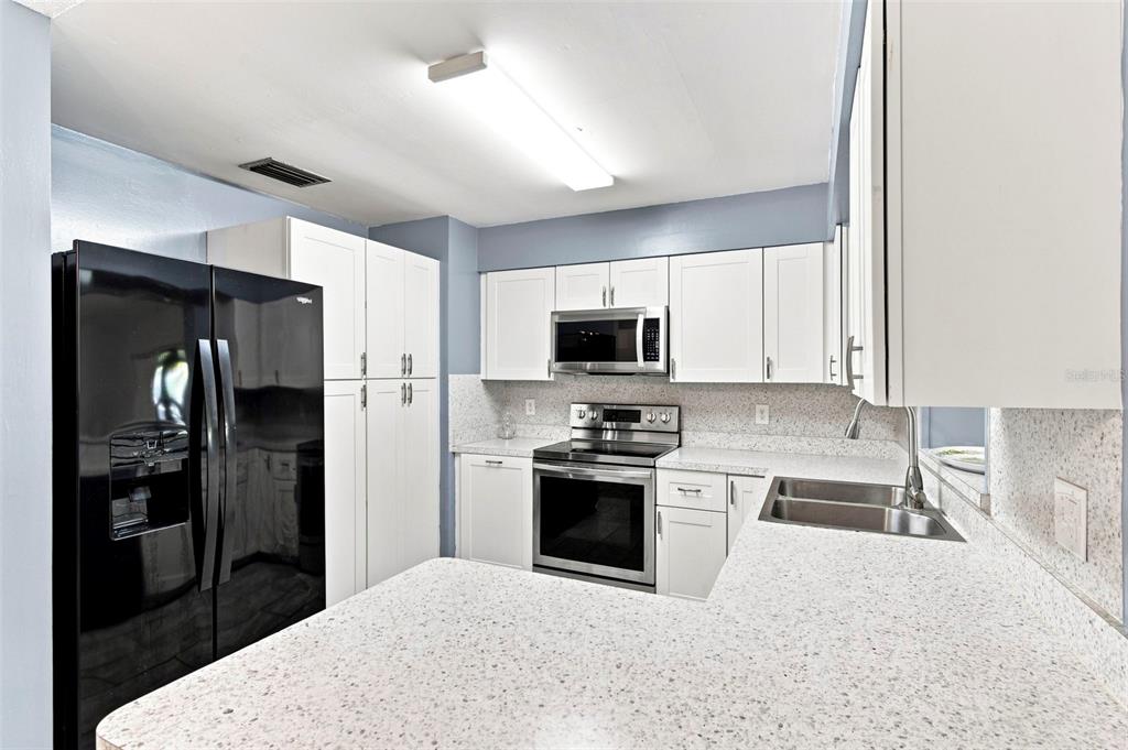 A kitchen features white cabinets, speckled countertops, stainless steel appliances, and a black refrigerator — 1655 N FLORAL AVENUE, BARTOW, FL
