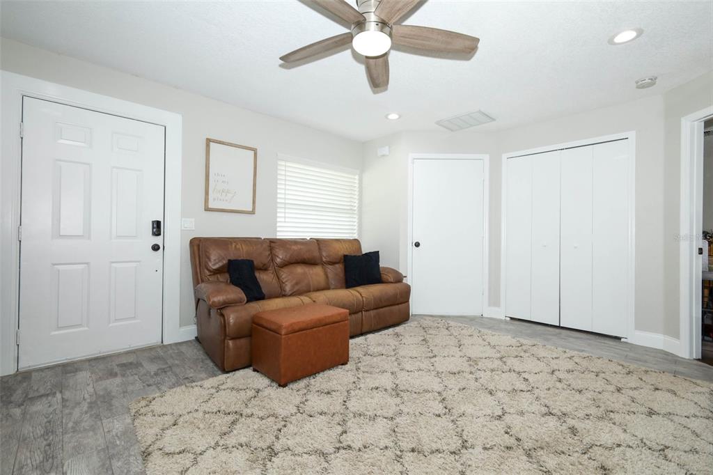 A living room with a brown leather sofa, matching ottoman, and light gray wood-look flooring — 738 E 11TH AVENUE, MOUNT DORA, FL