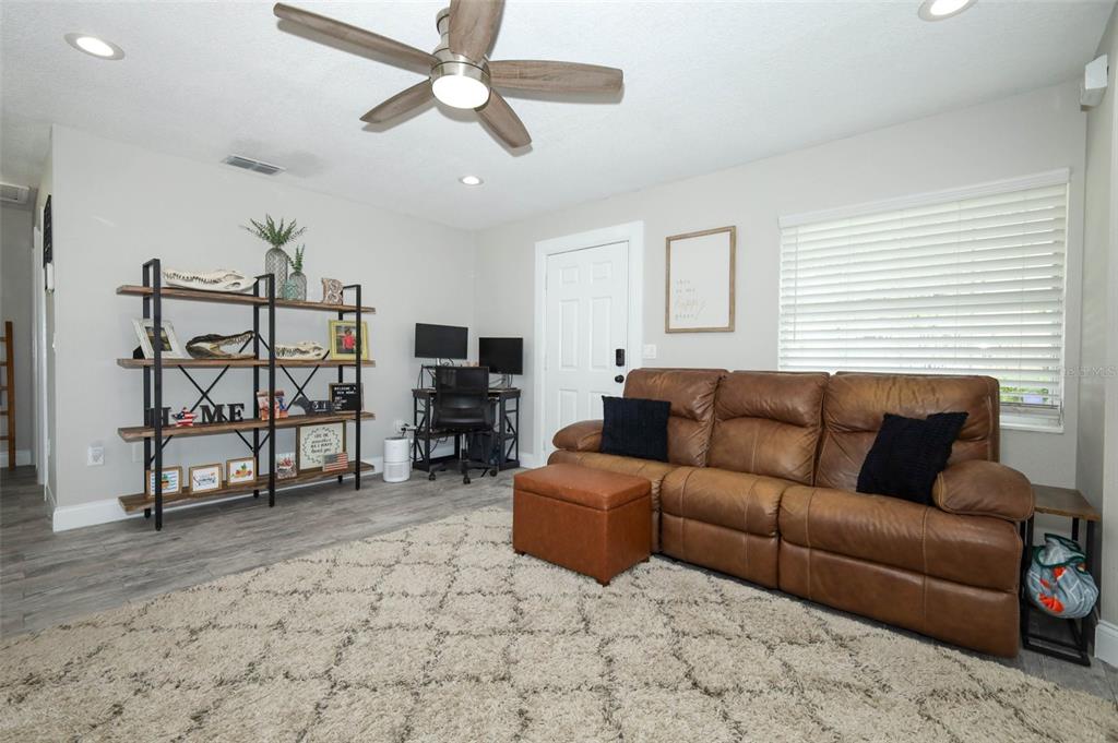 A living room features a brown leather sofa, a large area rug, and a shelving unit — 738 E 11TH AVENUE, MOUNT DORA, FL