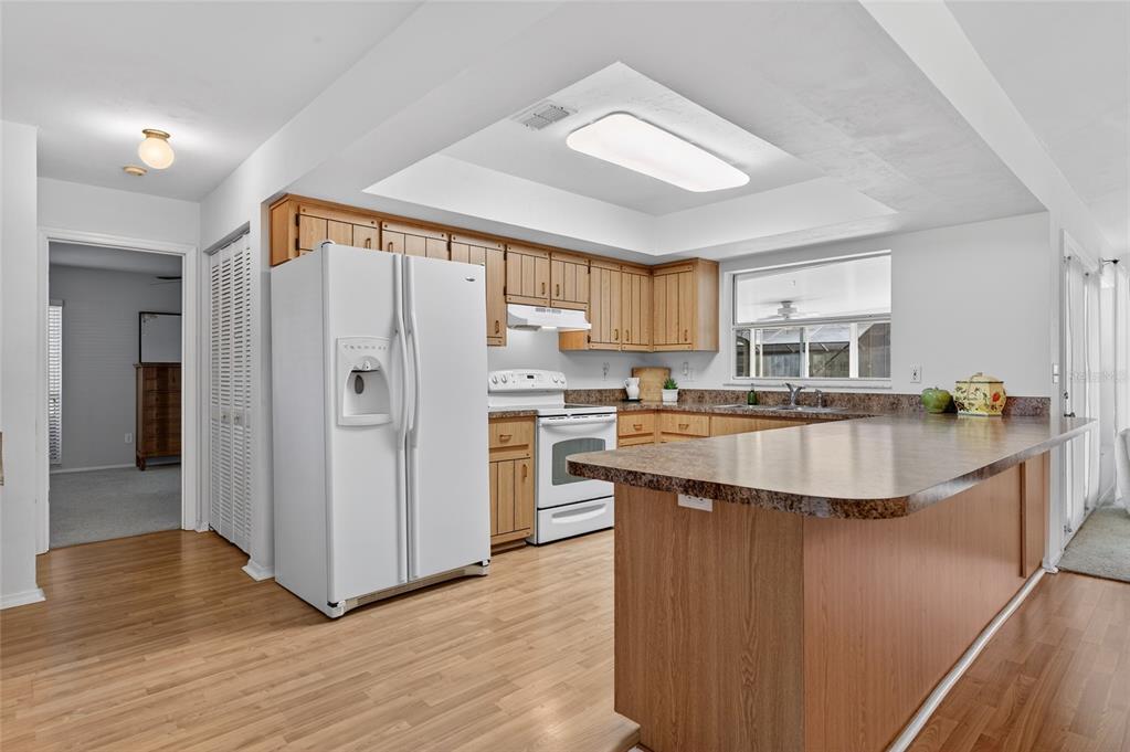 A kitchen features wood cabinets, white appliances, a breakfast bar, and light-colored wood flooring — 236 MEADOW LAKE DRIVE, EDGEWATER, FL