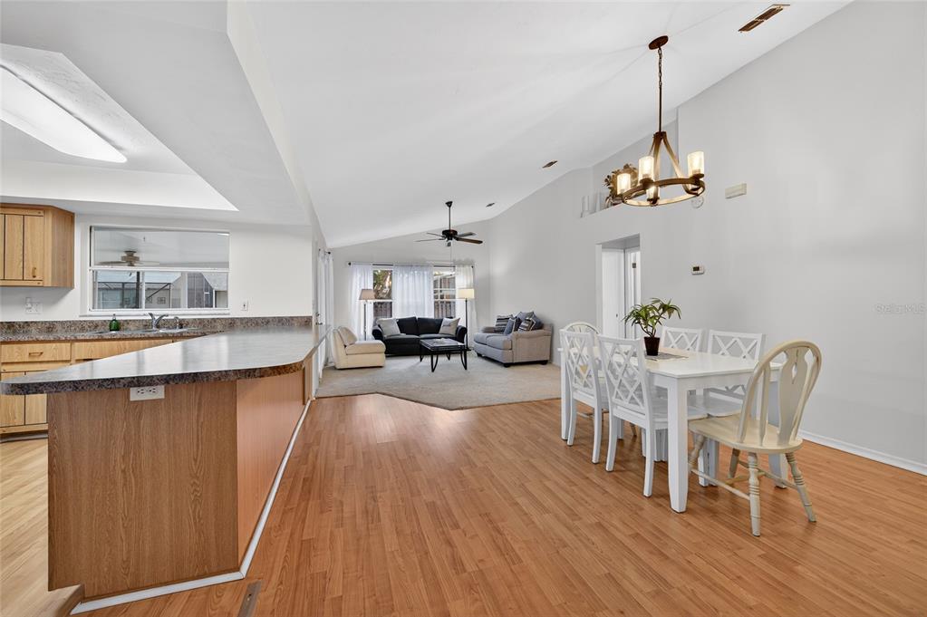 An open-concept living and dining area features wood-look flooring, a vaulted ceiling, and kitchen peninsula — 236 MEADOW LAKE DRIVE, EDGEWATER, FL