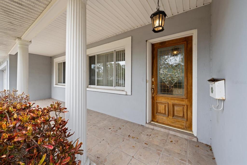 A covered front porch features tiled flooring, white columns, a wooden door, and a wall-mounted mailbox — 230 GARDEN CIRCLE, BELLEAIR, FL