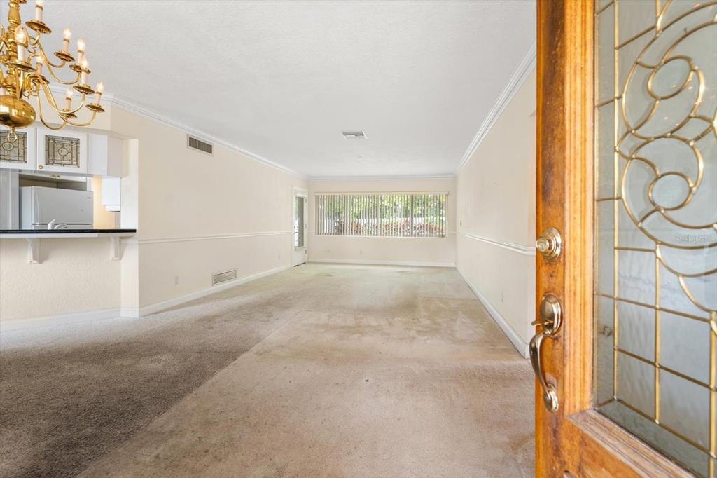 An interior view of a living room with carpeted floors, a chandelier, and a kitchen — 230 GARDEN CIRCLE, BELLEAIR, FL