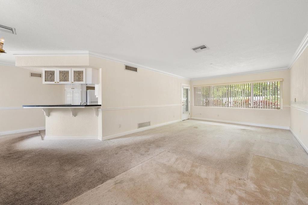 A living room features beige carpeting, a breakfast bar, and a large window with blinds — 230 GARDEN CIRCLE, BELLEAIR, FL