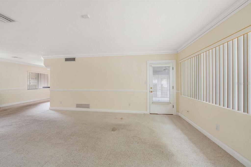 A carpeted living room features beige walls, a glass-paneled door, and vertical window blinds — 230 GARDEN CIRCLE, BELLEAIR, FL
