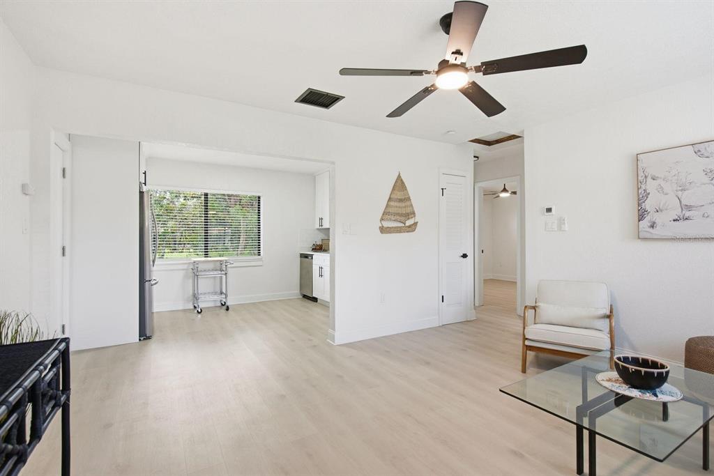 A bright living room with light wood flooring, a ceiling fan, and an adjacent kitchen — 5307 BERKLEY ROAD, NEW PORT RICHEY, FL