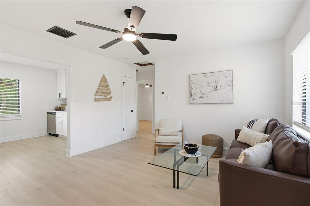 A living room with light wood floors, a ceiling fan, and a view into the kitchen — 5307 BERKLEY ROAD, NEW PORT RICHEY, FL