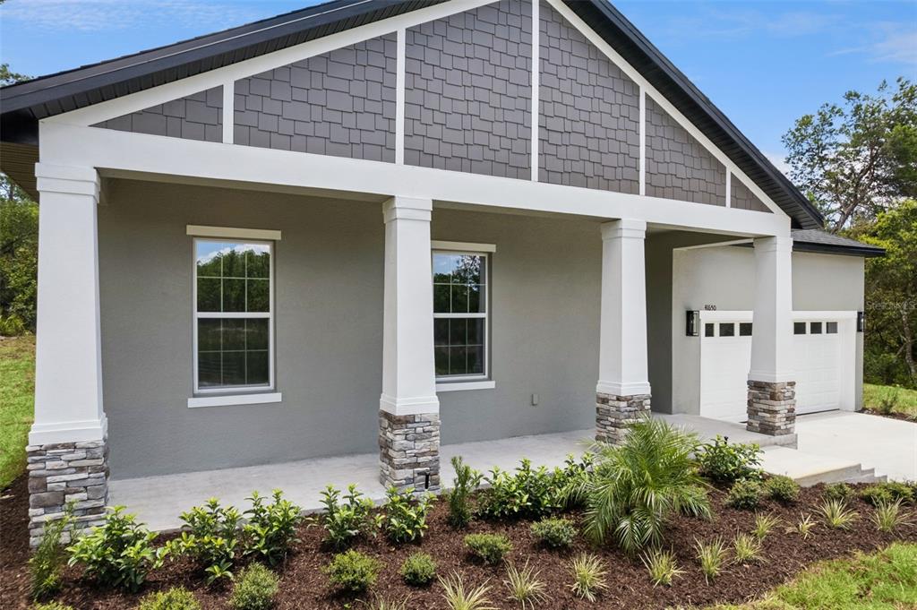 A gray house exterior features a covered porch with stone-based columns and shingled gables — 41650 LIGUSTRUM STREET, EUSTIS, FL