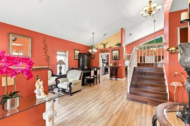 A living room with orange walls, wood flooring, a staircase, and a dining area — 84 KNIGHTS HOLLOW DRIVE, APOPKA, FL