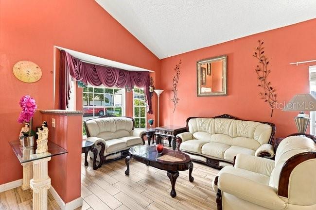 A living room with coral walls, a white sofa set, and a large bay window — 84 KNIGHTS HOLLOW DRIVE, APOPKA, FL
