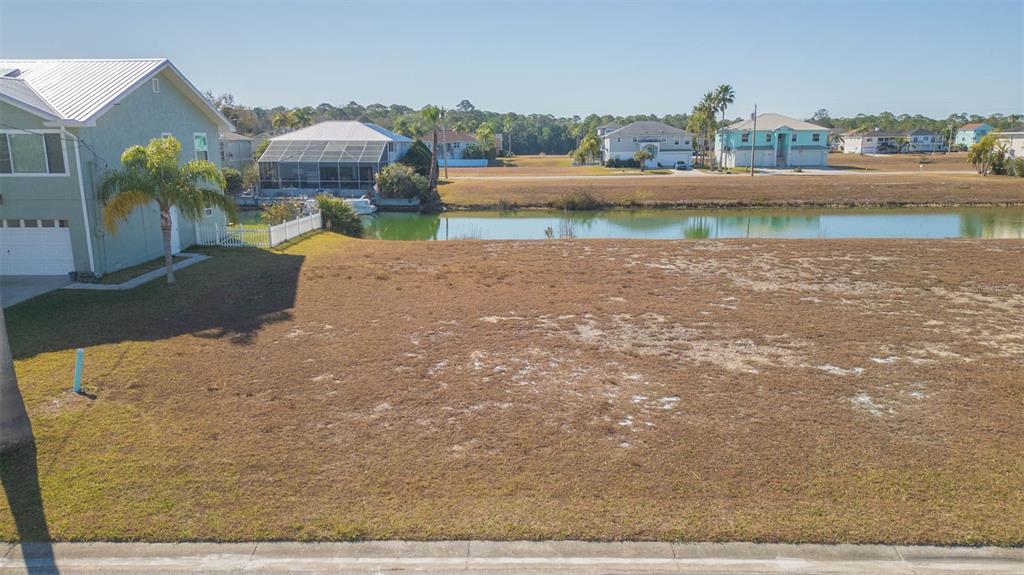A vacant, grassy waterfront lot sits next to a house with a palm tree — 3488 TRIGGERFISH DRIVE, HERNANDO BEACH, FL