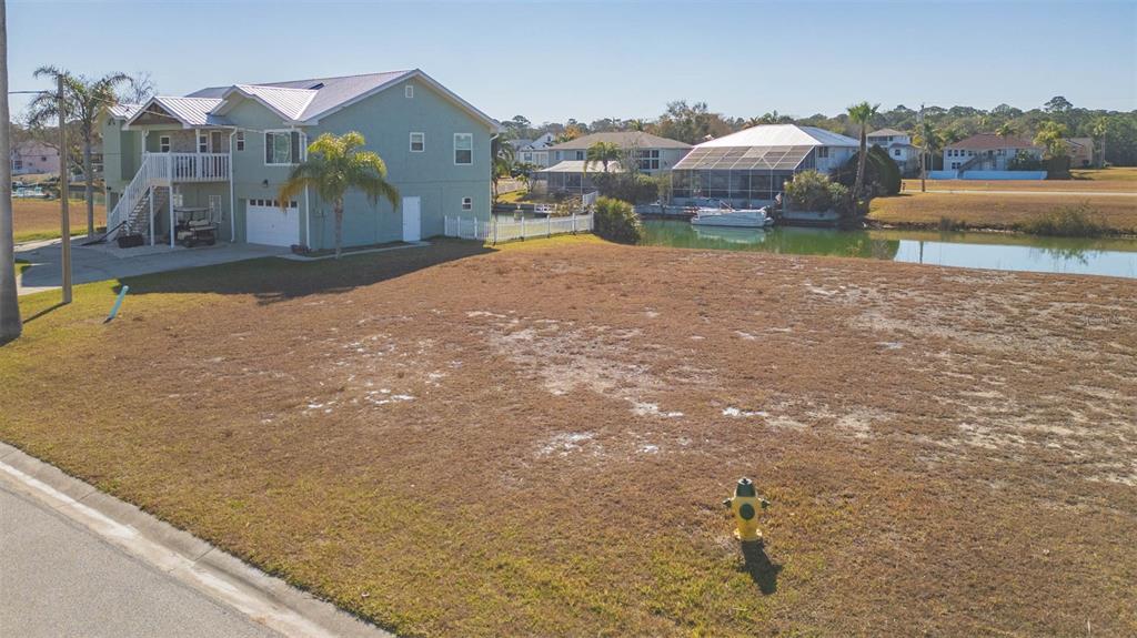 A vacant, grassy residential lot sits next to a two-story house and a canal — 3488 TRIGGERFISH DRIVE, HERNANDO BEACH, FL