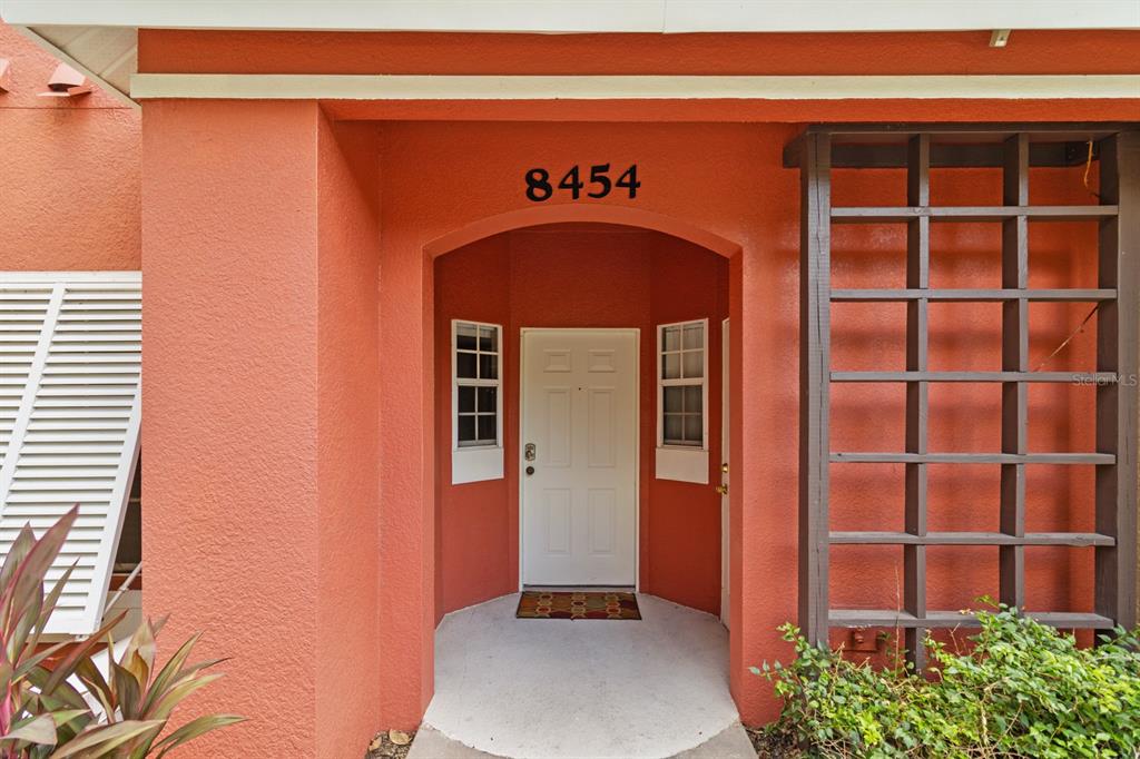 The exterior entrance of a home features a white door, side windows, and a trellis — 8454 CRYSTAL COVE LOOP, KISSIMMEE, FL