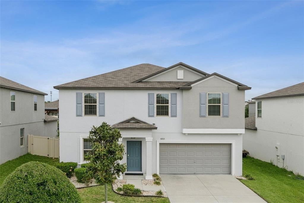 A two-story suburban house with light gray stucco, blue shutters, and a front garden bed — 4203 HANOVER DRIVE, NEW PORT RICHEY, FL