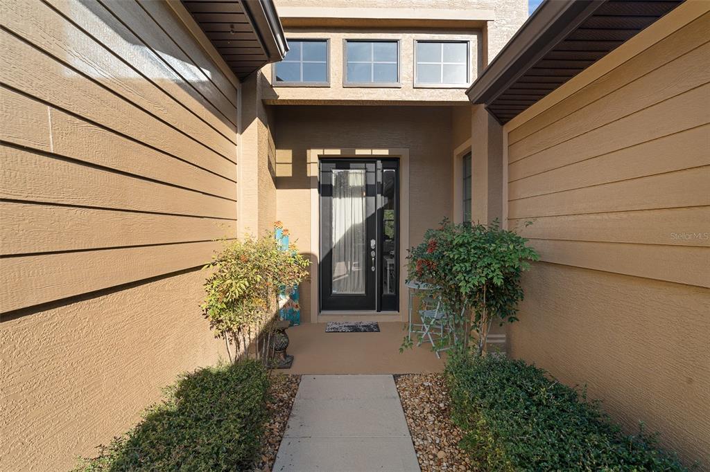 A concrete walkway leads to a front entrance with a black door and transom windows — 1047 KILKENNY LANE, ORMOND BEACH, FL