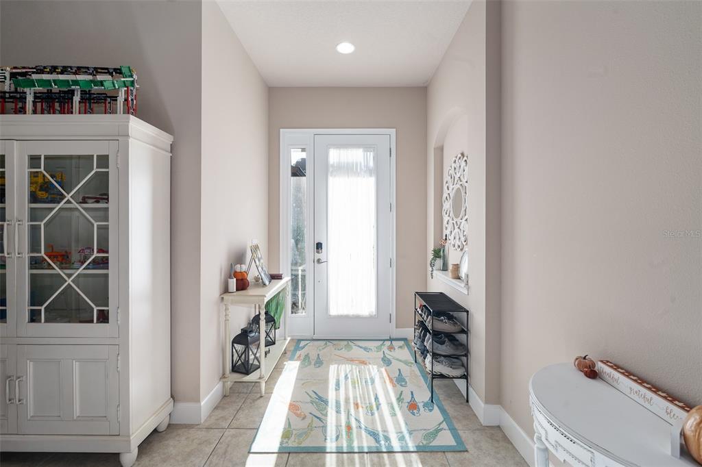 A bright entryway features tile flooring, a white front door, and a shoe rack — 1047 KILKENNY LANE, ORMOND BEACH, FL