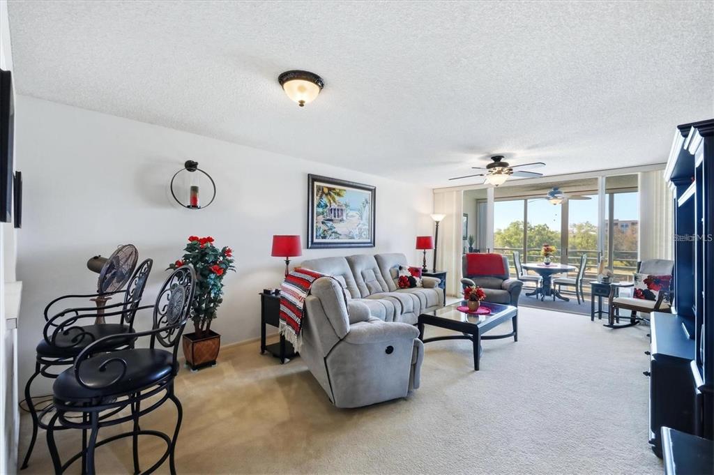 A living room features beige carpeting, a gray reclining sofa, and a balcony with seating — 4460 FAIRWAYS BOULEVARD UNIT 302, BRADENTON, FL