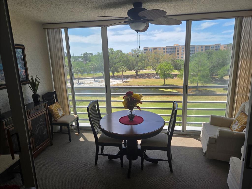 A sunroom features a round dining table, chairs, and large windows overlooking a golf course — 4460 FAIRWAYS BOULEVARD UNIT 302, BRADENTON, FL