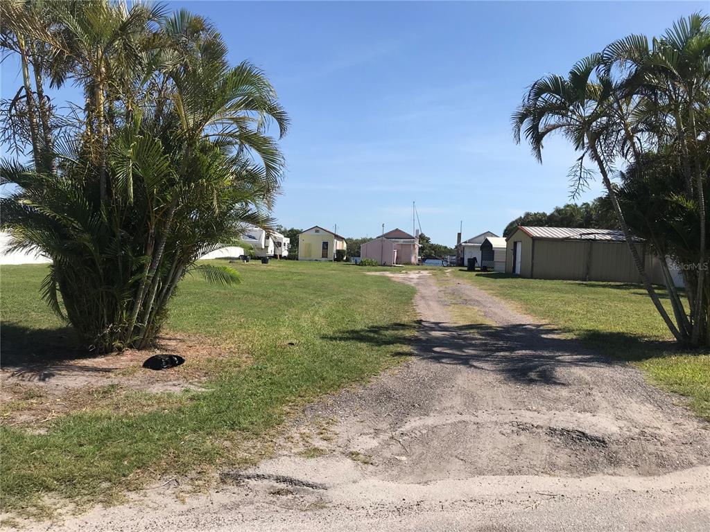 A gravel driveway leads toward several small buildings and a camper on a grassy lot — 3306 W SHELL POINT ROAD, RUSKIN, FL