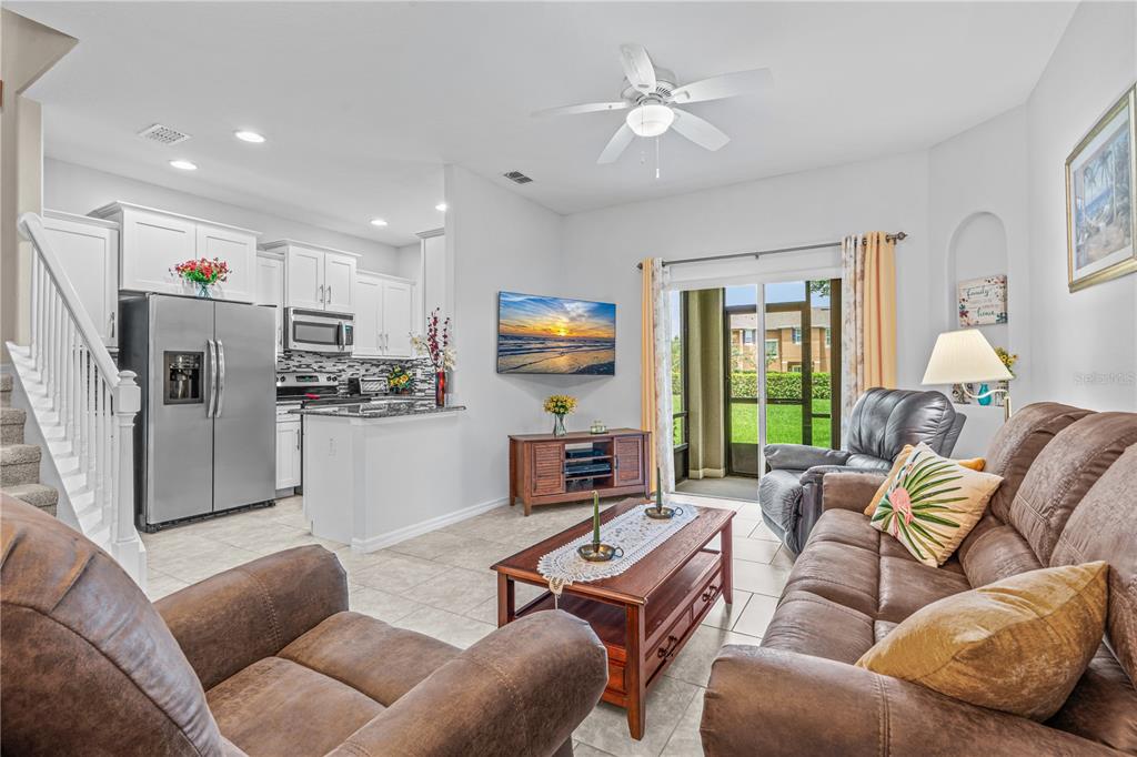 An open-concept living room and kitchen with tile flooring, a ceiling fan, and sliding doors — 104 MISTY GLEN LANE, DAYTONA BEACH, FL