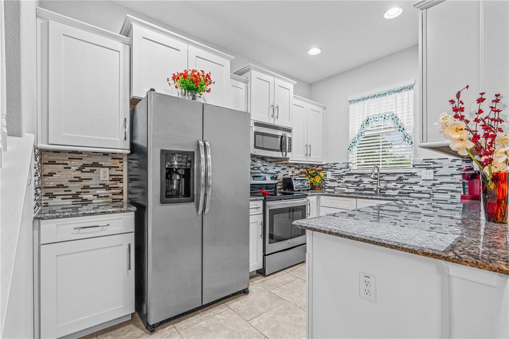 A kitchen with white cabinets, stainless steel appliances, granite countertops, and a mosaic tile backsplash — 104 MISTY GLEN LANE, DAYTONA BEACH, FL