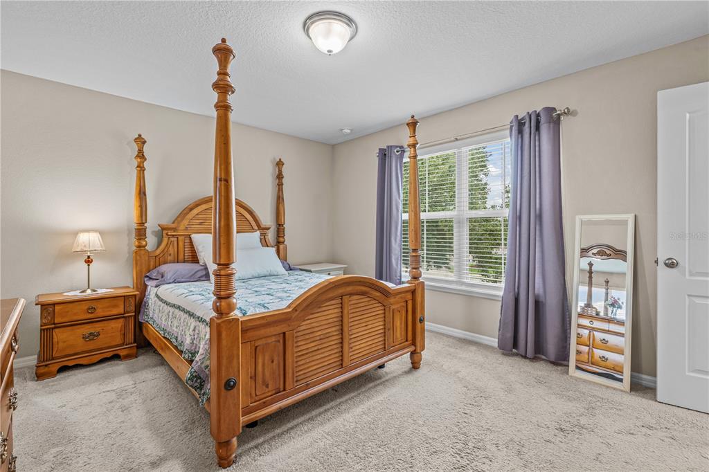 A bedroom features a wooden four-poster bed, a nightstand with a lamp, and a floor mirror — 104 MISTY GLEN LANE, DAYTONA BEACH, FL