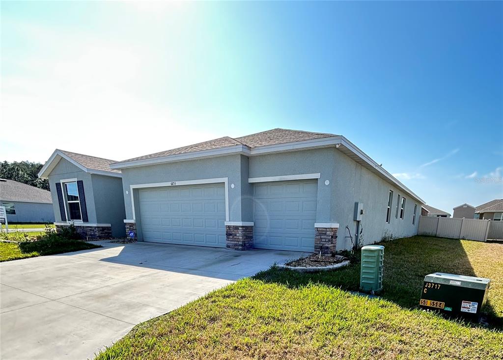 A gray, single-story house with a three-car garage and stone accents on the exterior — 6853 SE 3RD LOOP, OCALA, FL