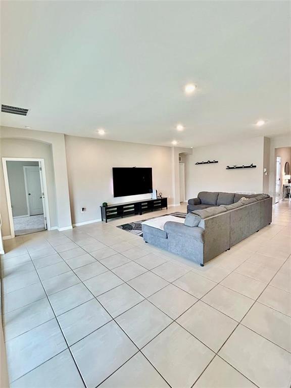 A spacious living room features light tile flooring, a large sectional sofa, and a wall-mounted television — 6853 SE 3RD LOOP, OCALA, FL